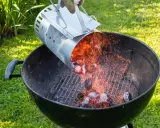 Encendiendo carbón con un chimenea para barbacoa. Chispas vuelan mientras se vierten las brasas calientes.