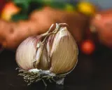 Czosnek dla koni, z widocznymi ząbkami i korzeniami, na ciemnym tle. W tle rozmyte pomarańczowe i czerwone kształty.