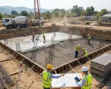 Obreros supervisan el vertido de hormigón en una obra, siguiendo el diseño de estructuras. Camión hormigonera y grúa en acción.