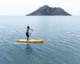 Chłopak na desce sup Aqua Marina przemierza spokojne morze w kierunku skalistej wyspy.