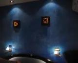 Pared azul con efecto veladura, dos cuadros abstractos y lámparas de pared.