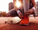 Frau bindet ihre neuen laufschuhe ein. Die Sonne scheint, ein Springseil liegt bereit.