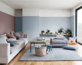 Soggiorno accogliente con divano beige, tappeto grigio e pareti color carta da zucchero. Un coniglietto curioso osserva dal cesto.