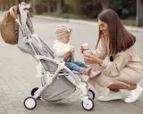 Mama karmi córeczkę z butelki, siedząc obok wózka. Idealne wózki dla dziewczynki na spacer.