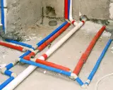 Skomplikowana instalacja wodociągowa z rurami w kolorach czerwonym, niebieskim i białym, przygotowana do ukrycia w ścianie.