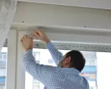 Hombre con camisa a cuadros midiendo para reparar persianas.