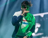 Raper w zielonej bluzie z napisem "Colette" śpiewa do mikrofonu. W tle zielone światła, jakby po influenza taco.