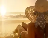 Donna con cappello di paglia e un bikini a pois, godendosi il tramonto sulla spiaggia. La sua pelle ha una perfetta abbronzatura arancione.