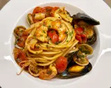 Spaghetti allo scoglio with shrimp, mussels, clams, squid, and cherry tomatoes in a white bowl.