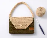 Bolso de trapillo bicolor, verde y beige, con asa y botón de madera. A su lado, ovillo de lana y ganchillo.