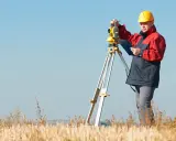 Geodeta w żółtym kasku pracuje z tachimetrem w polu. Zastanawiasz się, ile kosztuje geodeta?