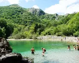 Gente disfrutando del agua cristalina en la olla de San Vicente, rodeada de exuberante vegetación y montañas.