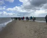 Folk promenerar längs en sandremsa vid vattnet norr om Skagen. Molnig himmel och hav.