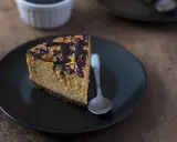 Tranche de cheesecake sans gluten sans lactose, nappée de chocolat noir, sur une assiette noire avec une cuillère.