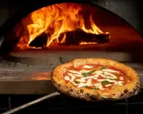 En perfekt italiensk pizza med mozzarella och basilika tas ur en vedeldad ugn med flammande eld.