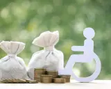 Pieniądze i symbol osoby na wózku inwalidzkim. Zastanawiasz się, ile wynosi świadczenie wspierające?