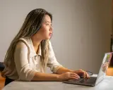 Młoda kobieta, analityk, skupiona na pracy przy laptopie. Jej wzrok skierowany jest w dal, jakby analizowała złożone dane.