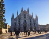 Le majestueux Duomo di Milano se dresse sous un ciel bleu, entouré de passants et d'un sapin de Noël décoré.