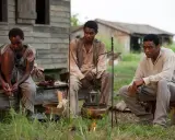 Tre persone sedute all'aperto, in un'ambientazione che ricorda i film biografici sulla schiavitù.
