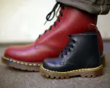 Ein roter und ein schwarzer Dr. Martens Stiefel, die die lange **Dr. Martens Geschichte** von robusten Schuhen für alle Generationen symbolisieren.