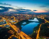 Widok z lotu ptaka na rozświetlone miasto nocą, z autostradą i trzema stawami w tle.