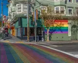 A vibrant rainbow crosswalk leads to a building adorned with a large rainbow mural, a symbol of the gay bed breakfast scene in San Francisco.