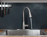 Moderner Küchenwasserhahn für Untertischboiler, der Wasser in ein Spülbecken laufen lässt. Messer hängen an der Wand.