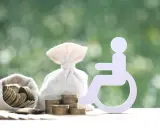 Symbol osoby na wózku inwalidzkim obok worków z pieniędzmi i monet. Symbolizuje wniosek o świadczenie wspierające.