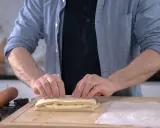 Un homme plie une pâte feuilletée professionnelle sur une planche en bois, prêt à créer des couches parfaites.