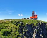 Widok na górskie **śnieżne kotły** z budynkiem obserwatorium na szczycie. Turyści spacerują po zielonych zboczach.