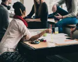 Eine Gruppe junger Leute arbeitet an einem Projekt. Eine Frau mit **Lernschwäche** hält einen Stift und erklärt etwas.