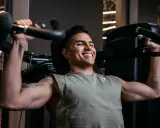 Ein Mann trainiert im Fitnessstudio, um seinen Brustmuskel aufzubauen. Er lächelt zufrieden, während er die Gewichte hebt.