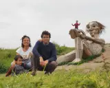 Familia disfrutando de Copenhague con niños, posando ante una escultura gigante de madera. Un niño pequeño juega en la mano de la figura.