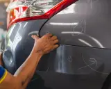 Ręce mechanika oceniają wgniecenia na karoserii samochodu, przygotowując się do usuwania uszkodzeń.