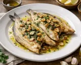 Lubina a la plancha con ajo laminado y perejil fresco, servida en plato blanco con aceite de oliva y limón al lado.
