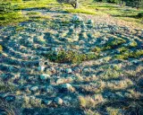 Stenlagd labyrint i Sverige, omgiven av gräs och buskar. Solen kastar långa skuggor över den uråldriga stensättningen.