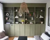 Une belle idée de bibliothèque salon avec des étagères vertes remplies de vases, plantes, livres et objets déco.