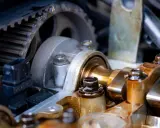 Zbliżenie na mechanizm rozrządu silnika, widoczny pasek zębaty i wałek rozrządu. Luźny pasek rozrządu objawy mogą być groźne dla silnika.