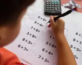 Dziecko zmagające się z zadaniami matematycznymi, być może z dyskalkulią. Widoczne są próby rozwiązywania przykładów i kalkulator.