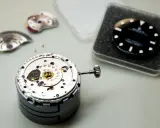 Parti di un movimento di orologio di lusso, tra cui il quadrante nero e la corona, pronti per l'assemblaggio.