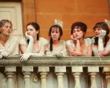 Cinque donne in abiti d'epoca, forse sorelle, riflettono su orgoglio e pregiudizio mentre guardano da un balcone.