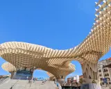 Der Metropol Parasol in Sevilla ragt mit seiner Holzkonstruktion in den blauen Himmel. Menschen steigen die Treppen hinauf.