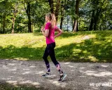 Frau läuft im Wald, um sich aufzuwärmen. Sonnenschein und grüne Bäume schaffen eine idyllische Kulisse für ihr Training.