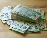 Stos banknotów 100 zł i 100 euro na drewnianym blacie. Może to być kwota na zasiłek stały.