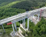 Wysoki wiadukt z betonowymi filarami, na którym widać ruch samochodowy. Konstrukcja z betonu C30/37 wznosi się nad zielonym lasem.