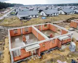 Budowa osiedla domów jednorodzinnych. Fundamenty i ściany parteru wznoszone z cegły, w tle gotowe domy. To początek drogi, jak zostać deweloperem.