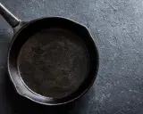 Eine schwarze Stahlpfanne, bereit für das Einbrennen, liegt auf einer dunklen, texturierten Oberfläche.