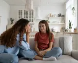 Matka próbuje rozmawiać z córką, która przeżywa bunt 11 latka. Dziewczynka siedzi z założonymi rękami, patrząc w bok.