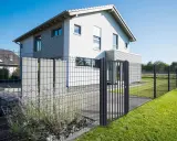 Maison moderne avec portail et pose grillage rigide, délimitant un jardin verdoyant.