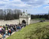 Pielgrzymka wchodzi przez zabytkową bramę. W oddali widać krzyż i piękne krajobrazy, które są nowa słupia atrakcje.